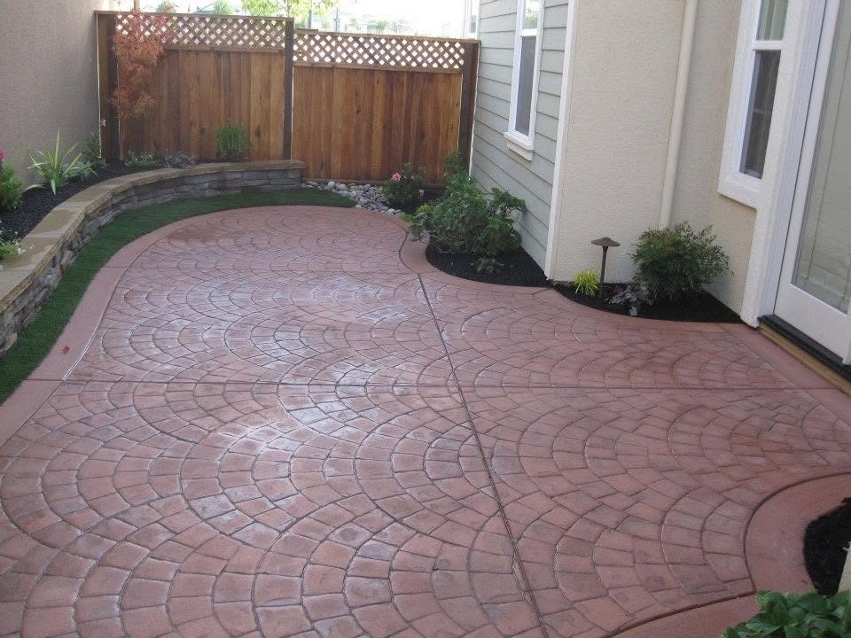 Terracotta-colored stamped concrete patio with a fan pattern beside a stacked stone wall