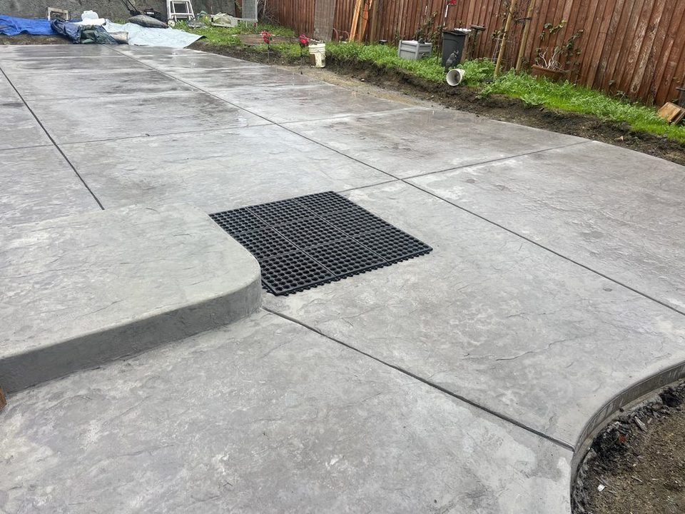 Concrete patio with an area drain grate set into the slab beside a wood fence