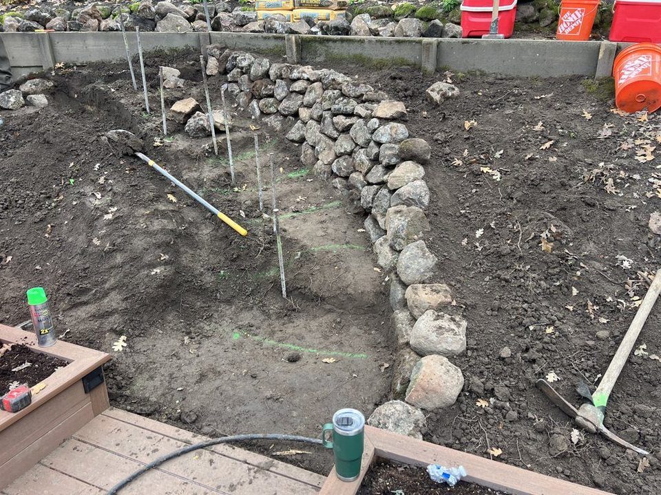Rock-edged drainage swale in dug soil with stakes and string lines before planting