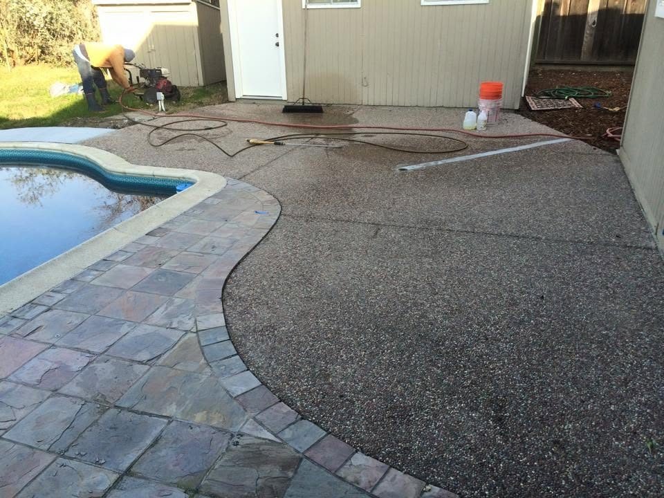 Exposed aggregate patio curving beside a backyard pool with a paver border