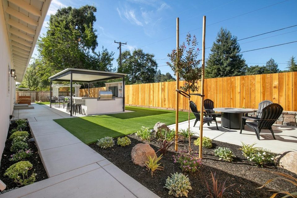 Fire table and outdoor chairs on a concrete patio beside a lawn and covered cabana