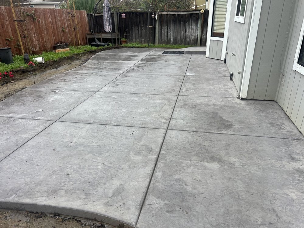 Gray concrete patio with saw-cut joints beside a wood fence