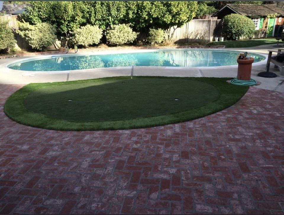 Round turf area beside a brick paver pool deck and swimming pool