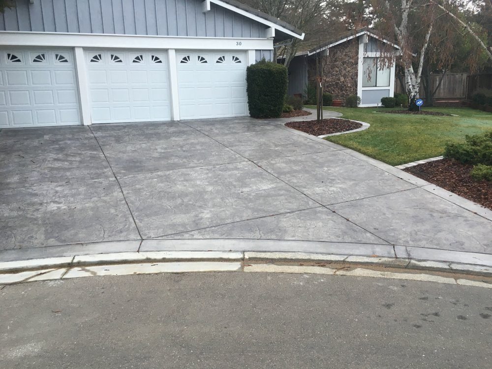 Gray concrete driveway in front of a three-car garage with a curb