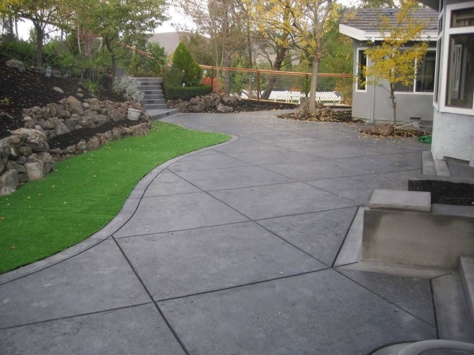 Charcoal-colored concrete patio with saw-cut joints and a curved turf edge