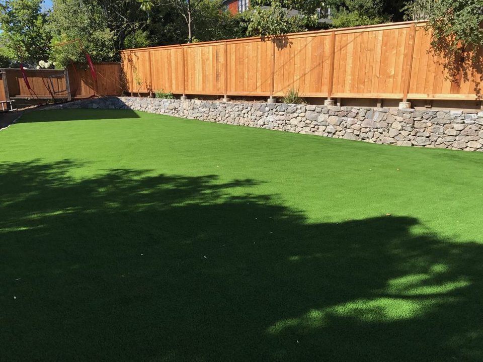 Synthetic turf lawn beside a wood fence and stone retaining wall