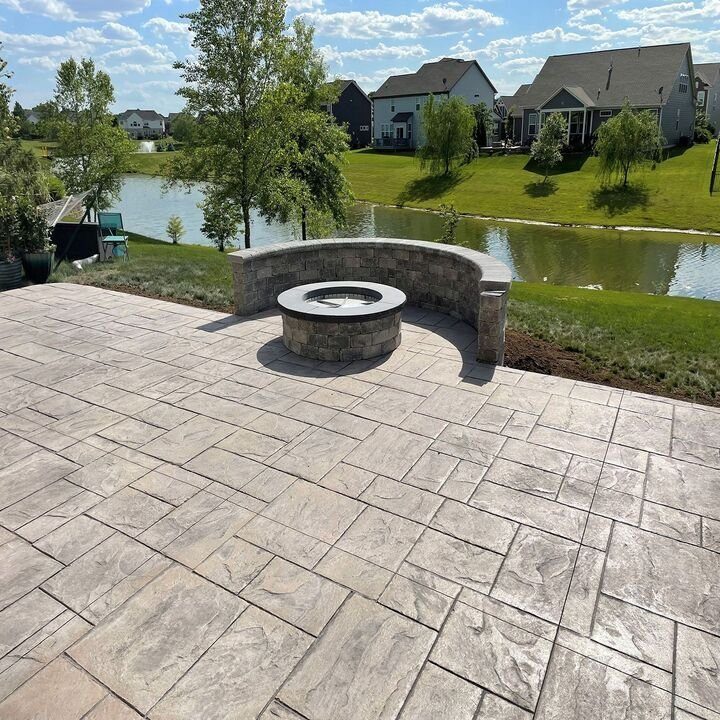 Stamped concrete patio with a round fire pit and curved stone seat wall beside a lawn