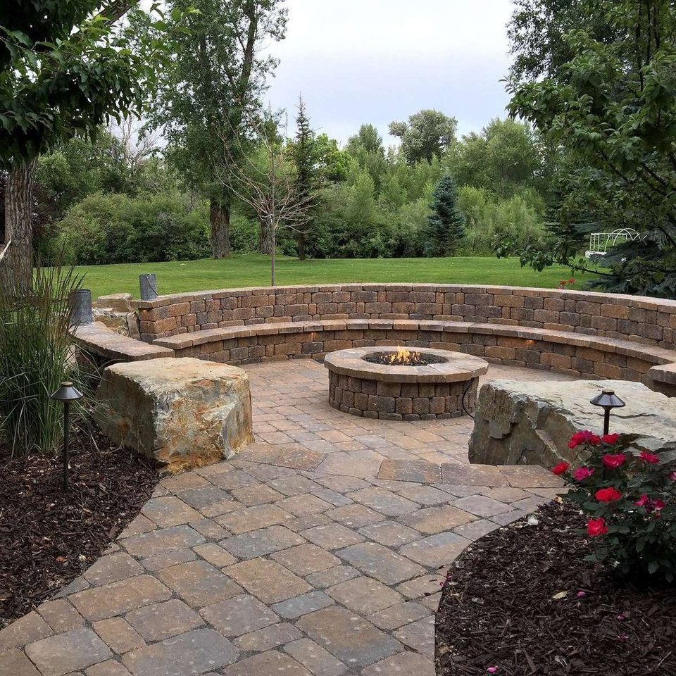 Circular fire pit with a curved stone seat wall and boulders on a paver patio