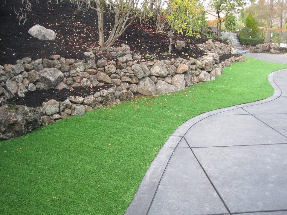 Curved turf strip alongside a concrete walkway and rock retaining wall