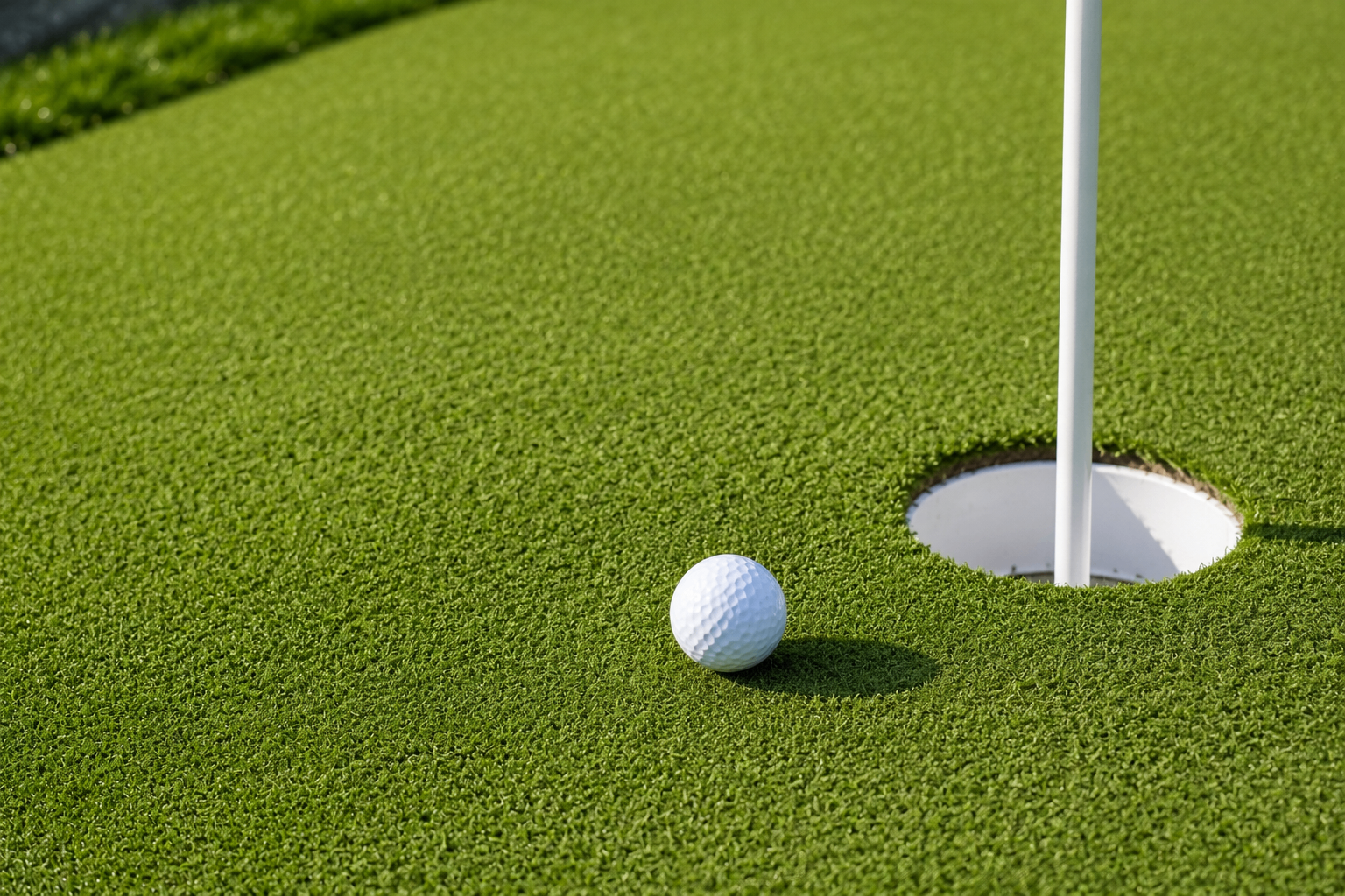 Close-up of a regulation cup and flag on a synthetic-turf putting green in Alamo