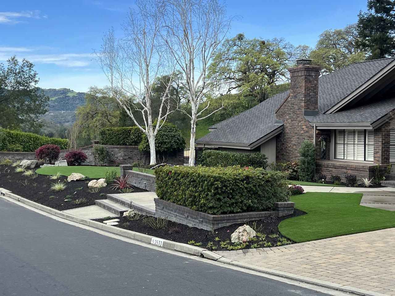 Paver driveway with a synthetic turf inlay strip and low retaining walls beside a home